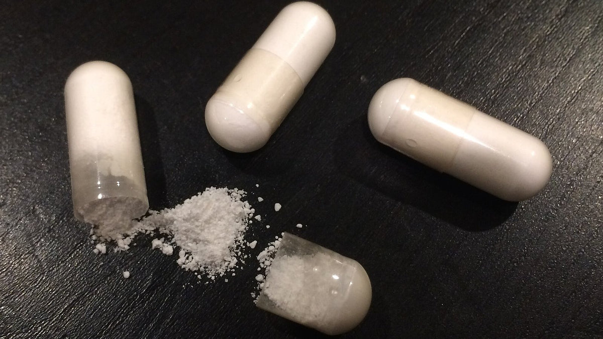 White capsules, one opened, with powder on a dark surface